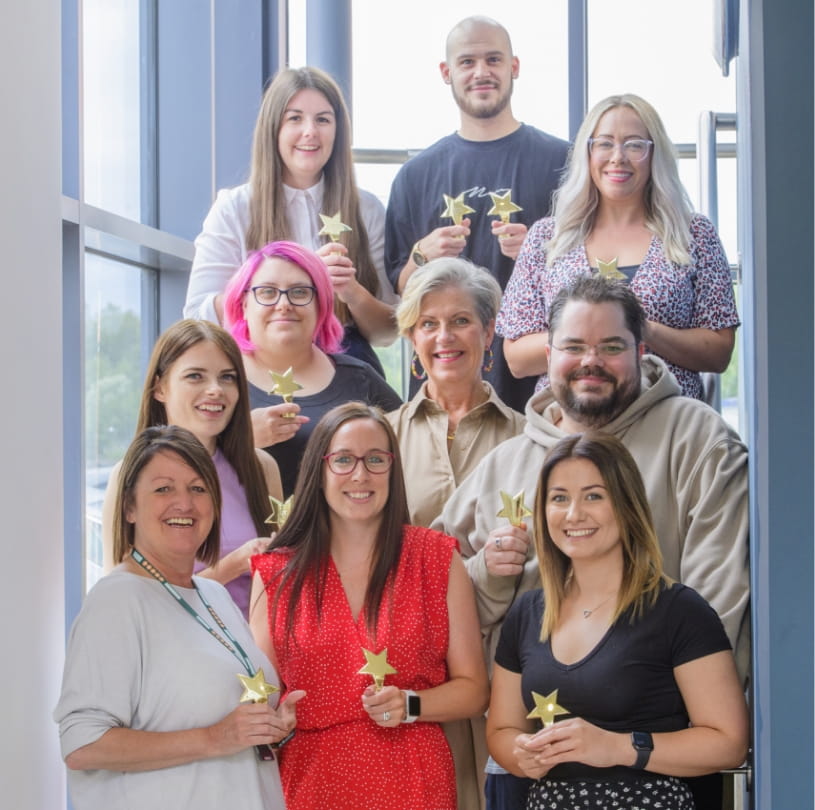 Our award winners. This image displays 11 of our team members, smiling, standing on a set of stairs holding their various awards.