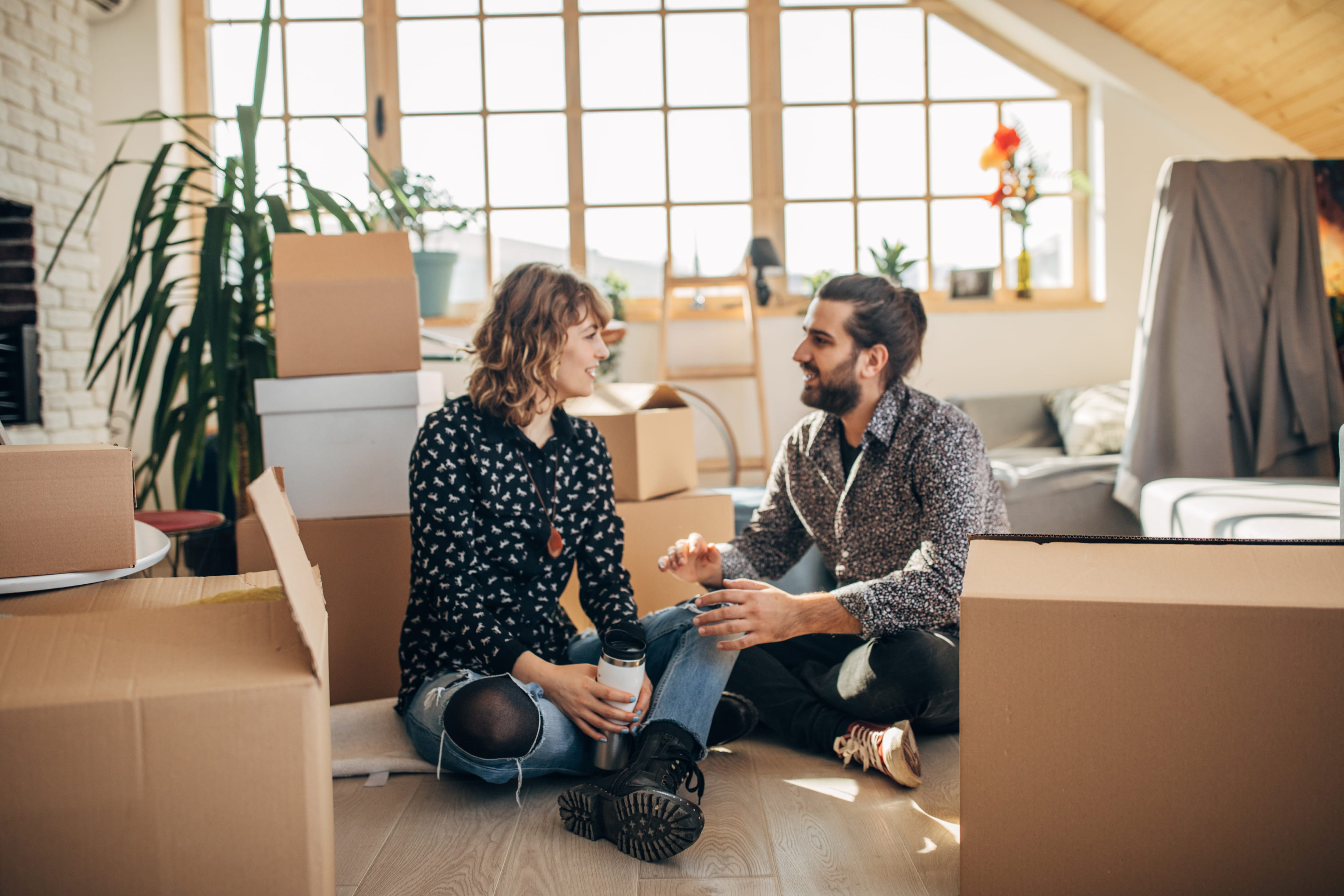 This image shows two people seated on the floor, surrounding by packing boxes. They are talking and smiling.