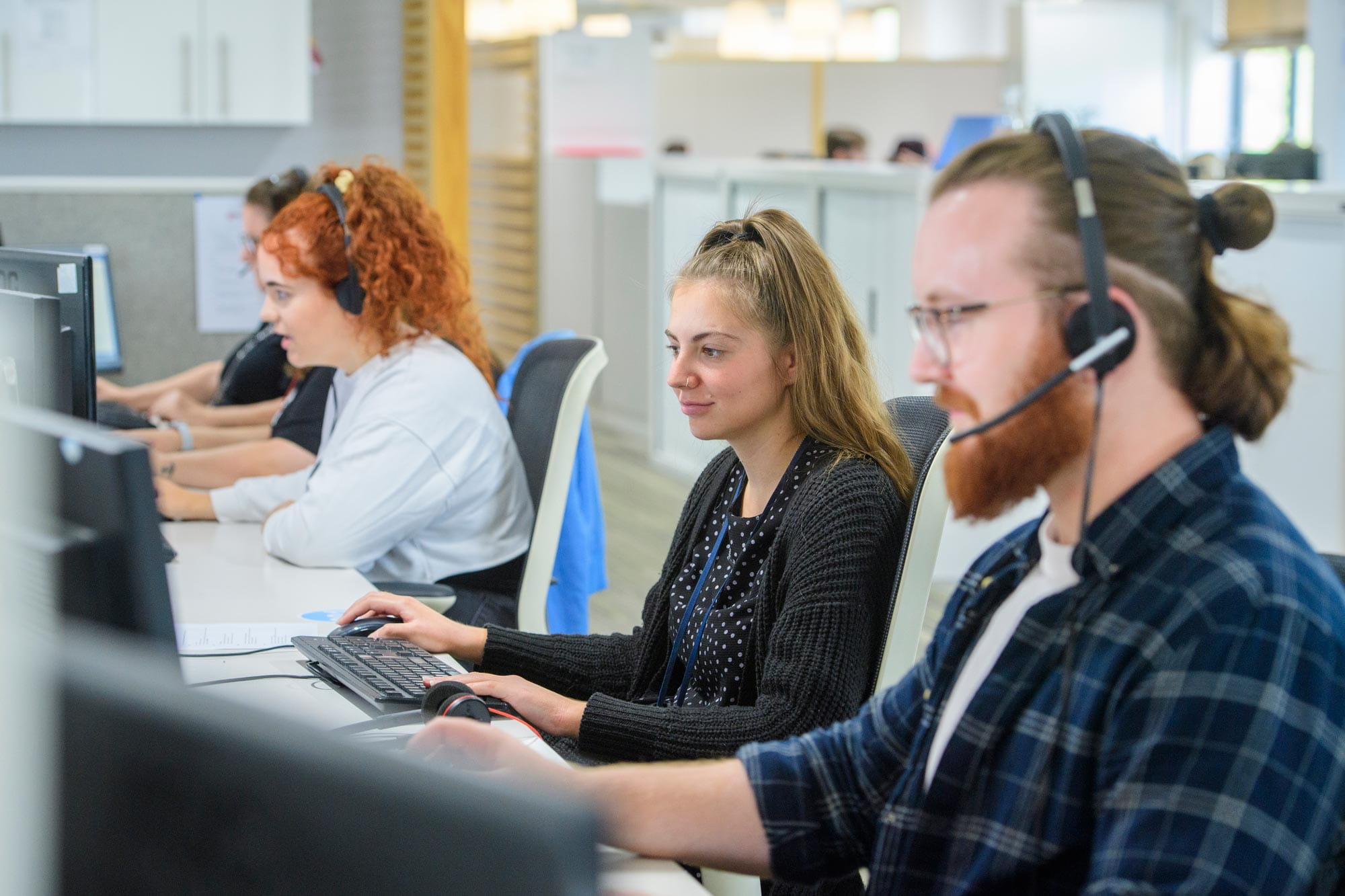 Contact us. This image shows 3 people working at desks in our call centre. Two of them are wearing headsets, the third is typing on a keyboard.