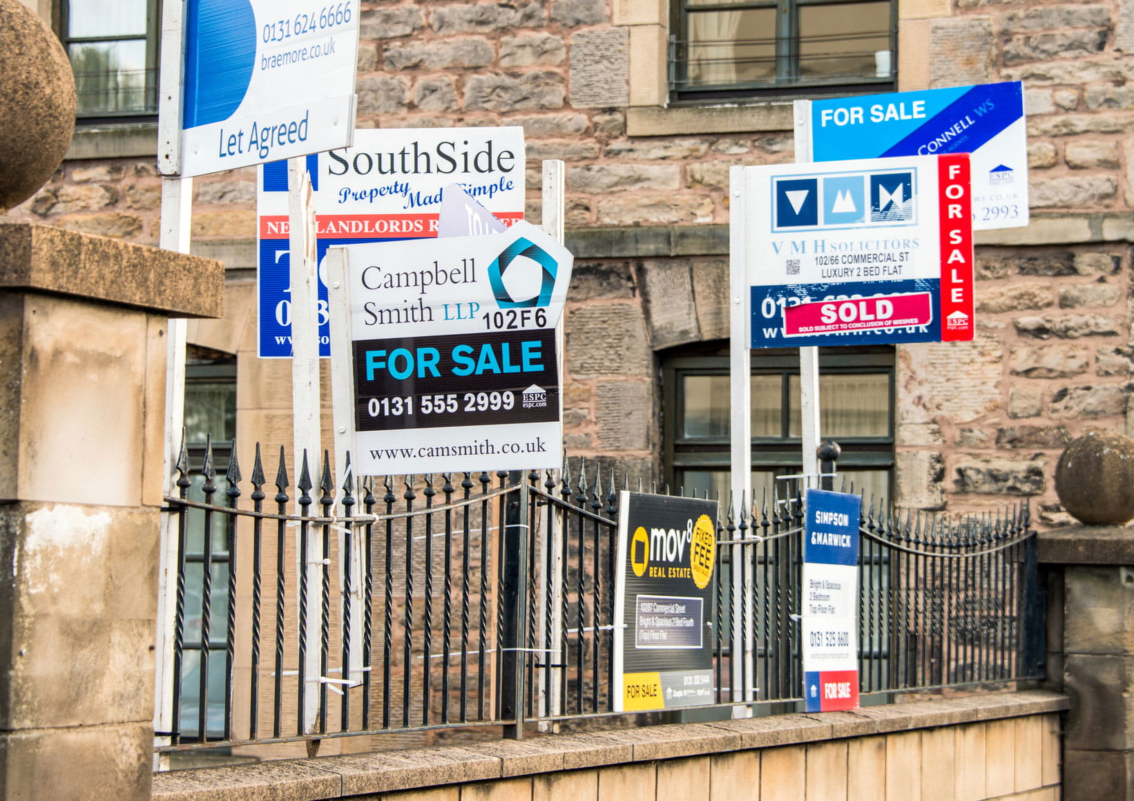 Landlord insurance. A person smiling and talking on their phone. In front of them is a table or desk with a coffee cup, a laptop and a glass of water.