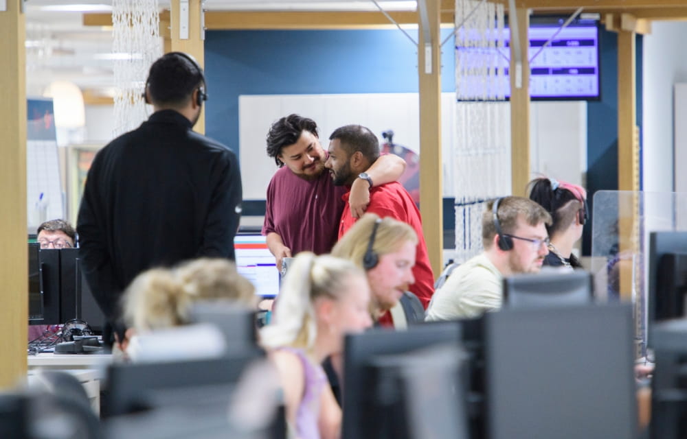 This image depicts two people celebrating in an office, in the foreground there are more people working in a call centre.