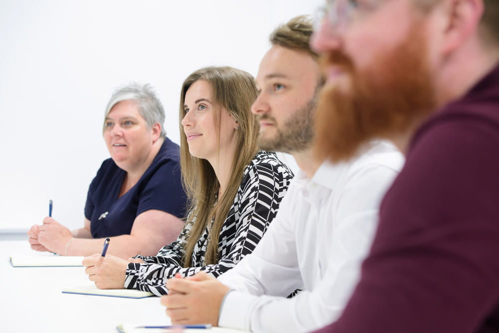 This photo depicts 4 of our team members sitting in a line during a meeting.