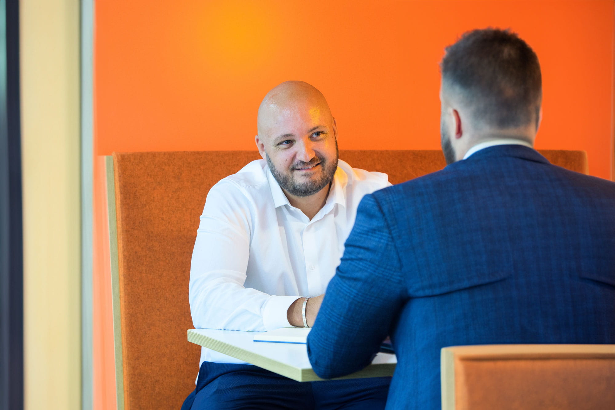 This depicts two people having a meeting, the wall in the background is bright orange.