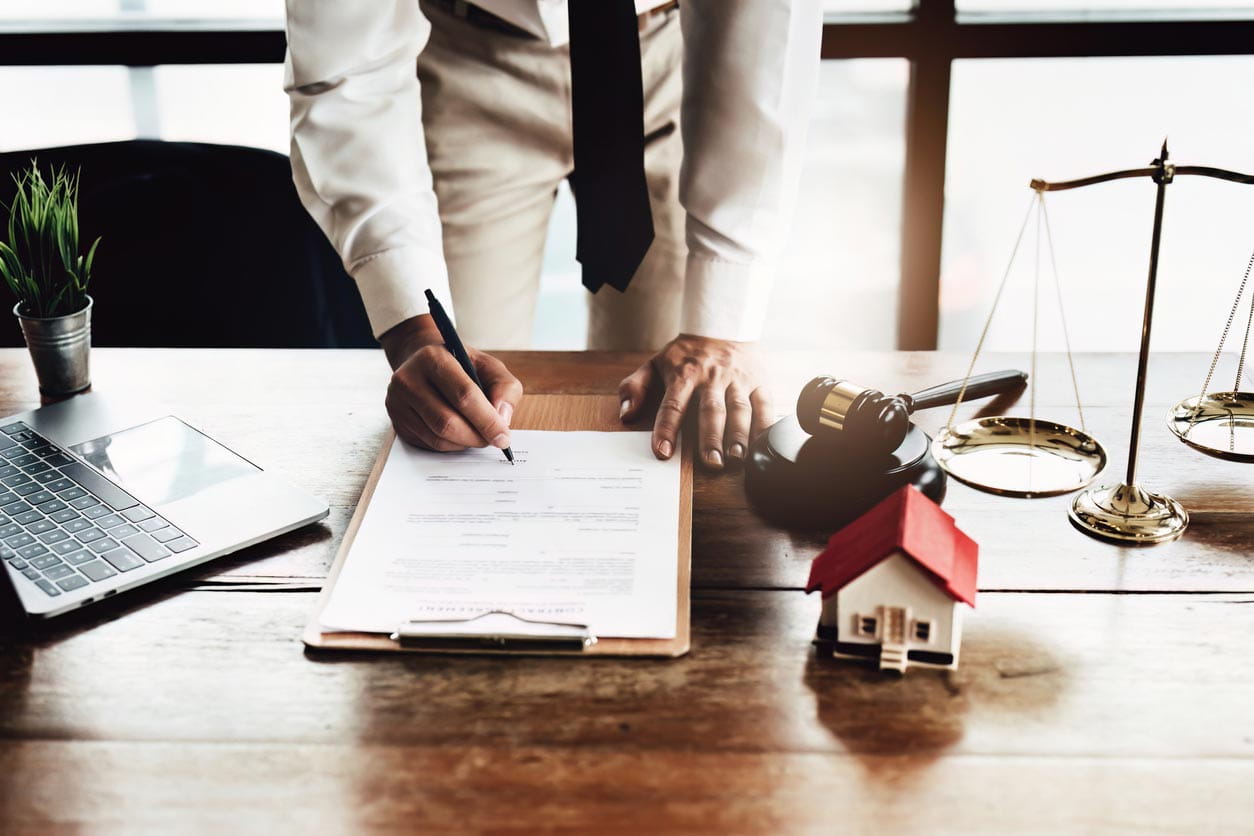 This is a photo of someone signing a document that is sitting on a desk, we can't see their face.