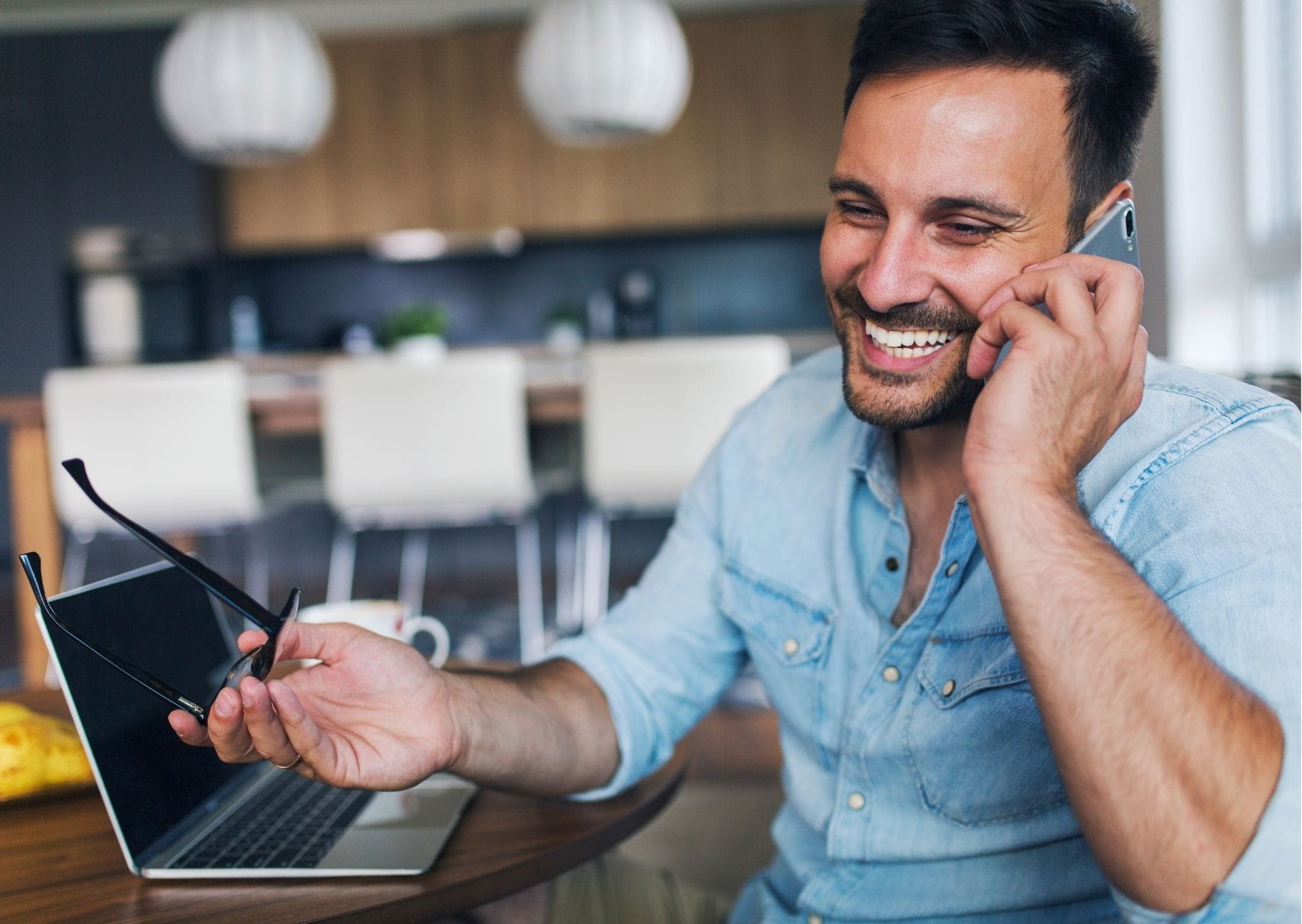 This is a photo of a man talking on a mobile phone, there is an open laptop next to him.