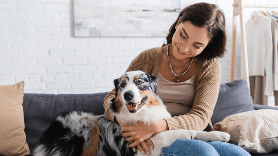 This photo shows a woman sitting on a sofa cuddling her dog.