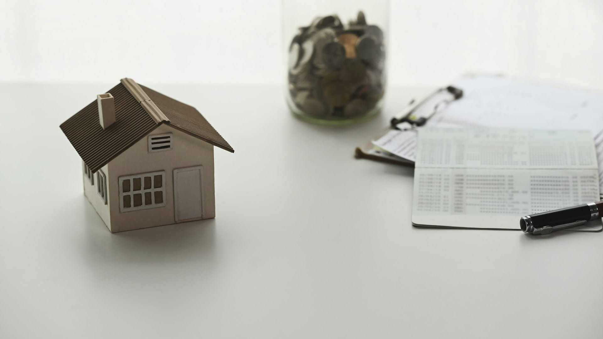 A small model of a house next to a jar of coins and a tenancy agreement form.