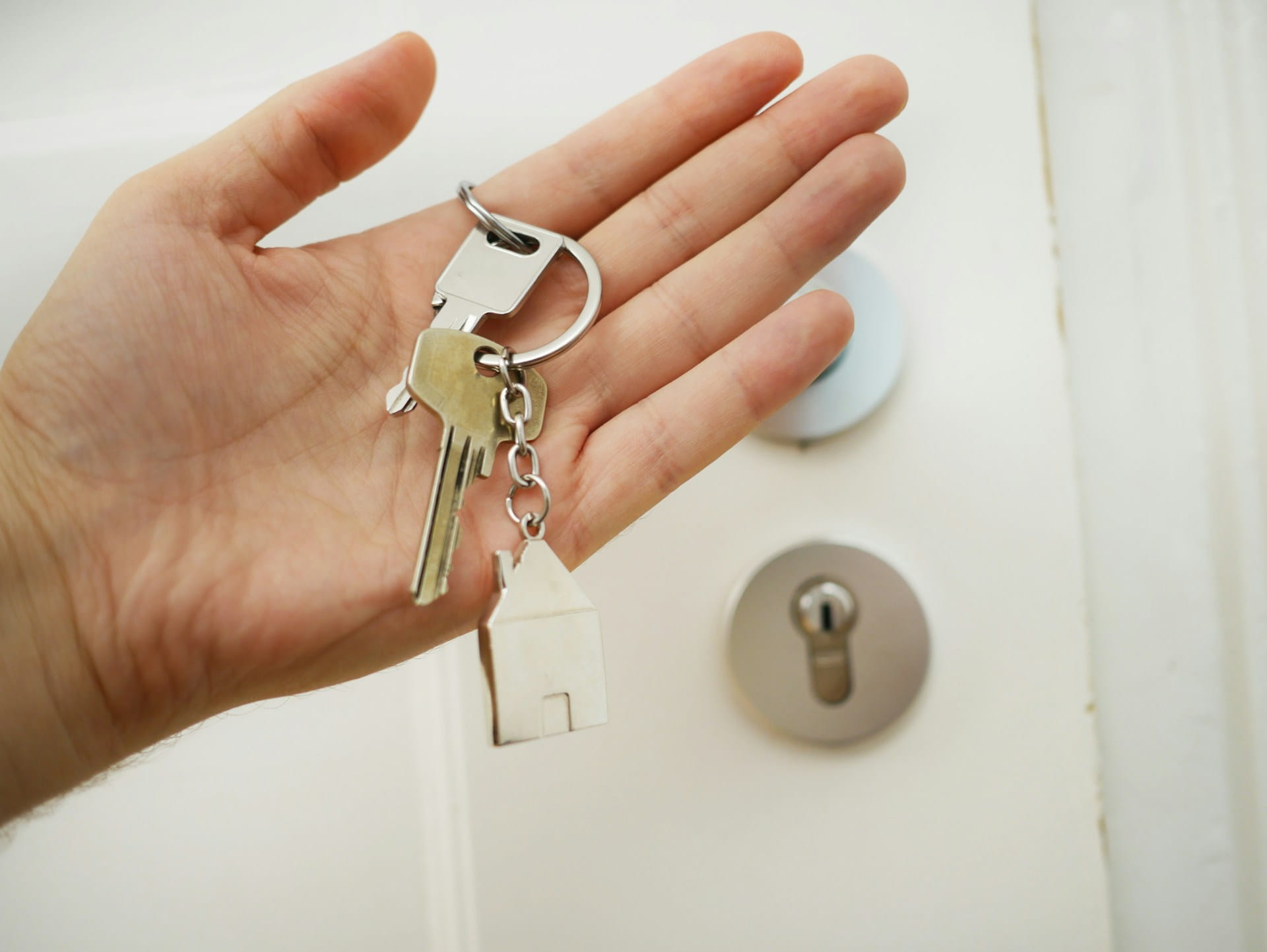 A landlord's hand holding the keys to their property in front of the property entrance.